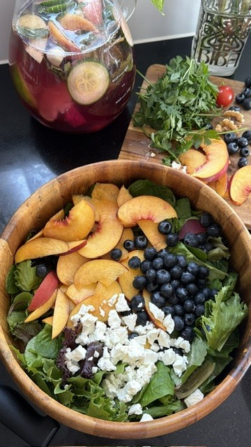 Peach blueberry and feta salad served in a wooden bowl beside fresh ingredients