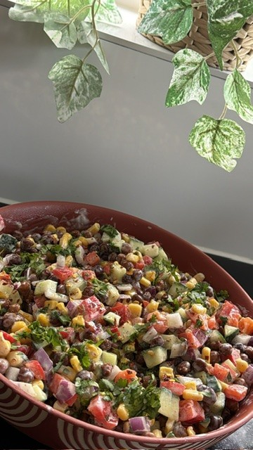Close-up of creamy black chickpea salad with sweetcorn, cucumber, red pepper, red onion, coriander and walnuts