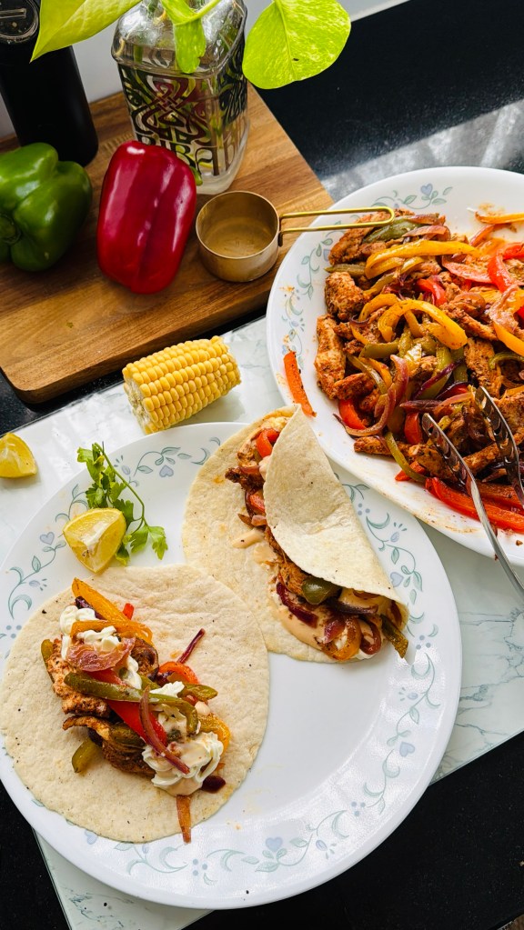 Chicken fajitas served in tortilla wraps with spicy mayo and plain mayo, next to a platter of fajita chicken and corn on the cob