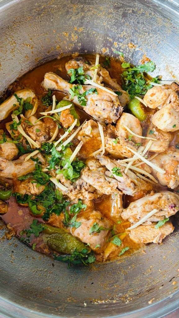 Close-up of chicken karahi in its tomato and yogurt masala, garnished with ginger slivers and fresh coriander