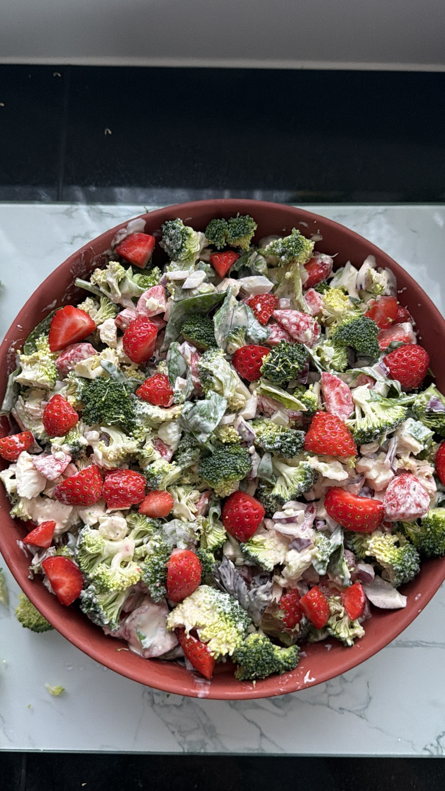 A bowl of creamy broccoli and strawberry salad with red onion and feta