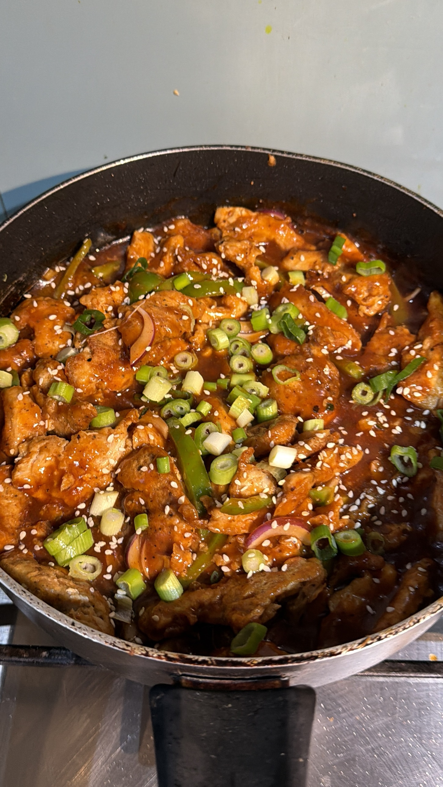Close-up of dragon chicken with capsicum, red onion, sesame seeds and green onion
