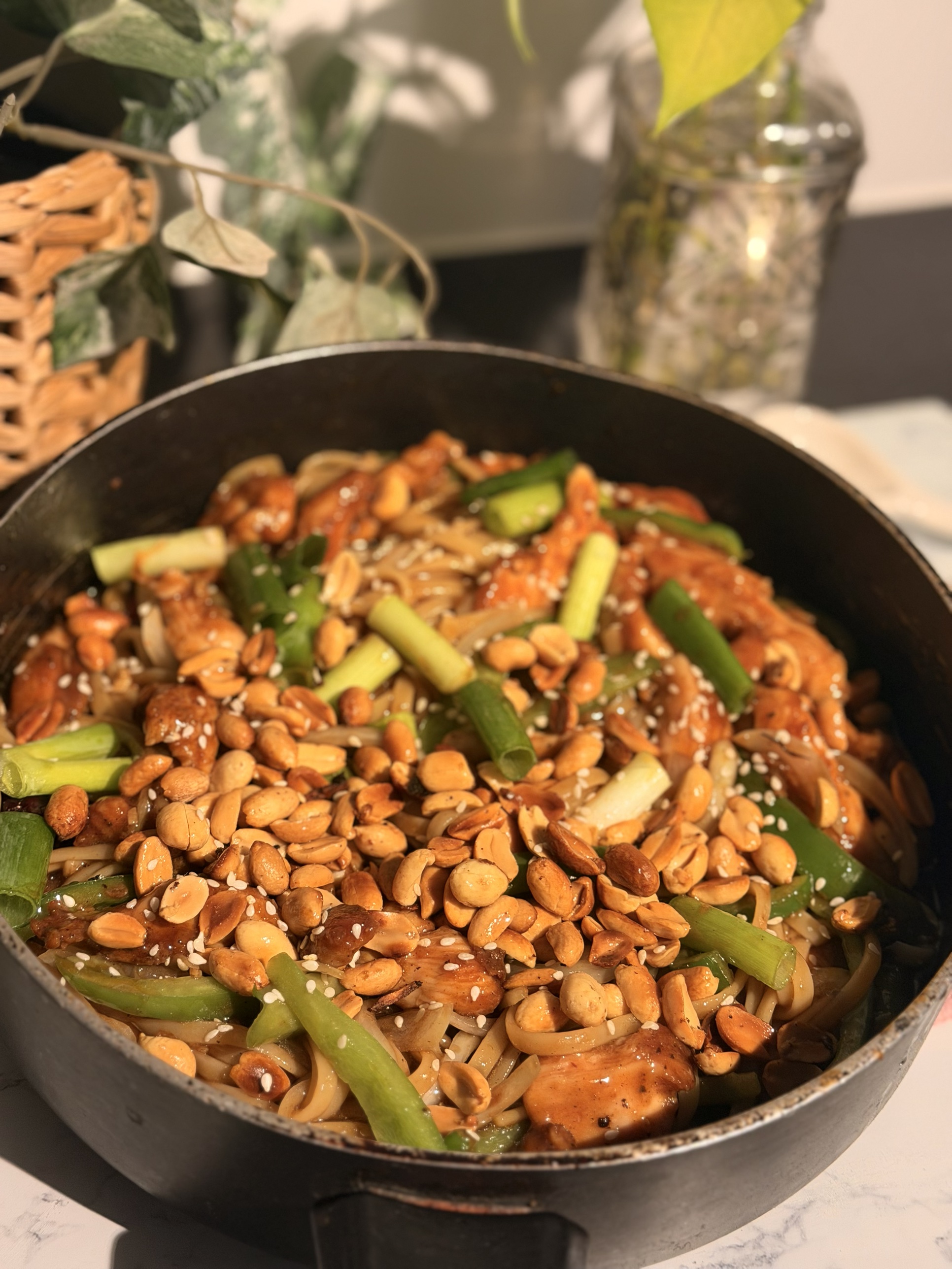 A pan of kung pao chicken noodles with peanuts, capsicum and green onion