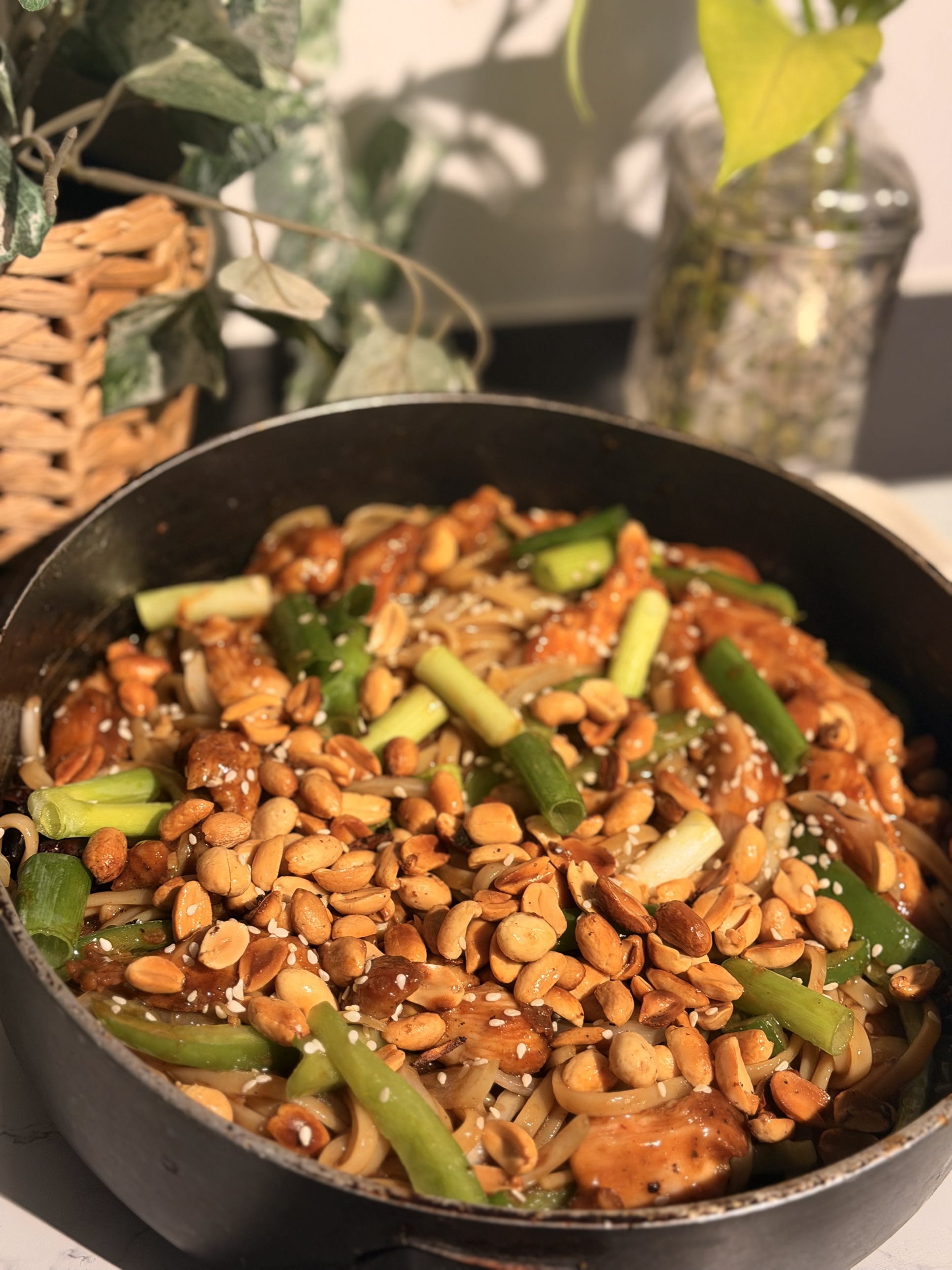 Kung pao chicken noodles in a pan, topped with peanuts, green onion and sesame seeds